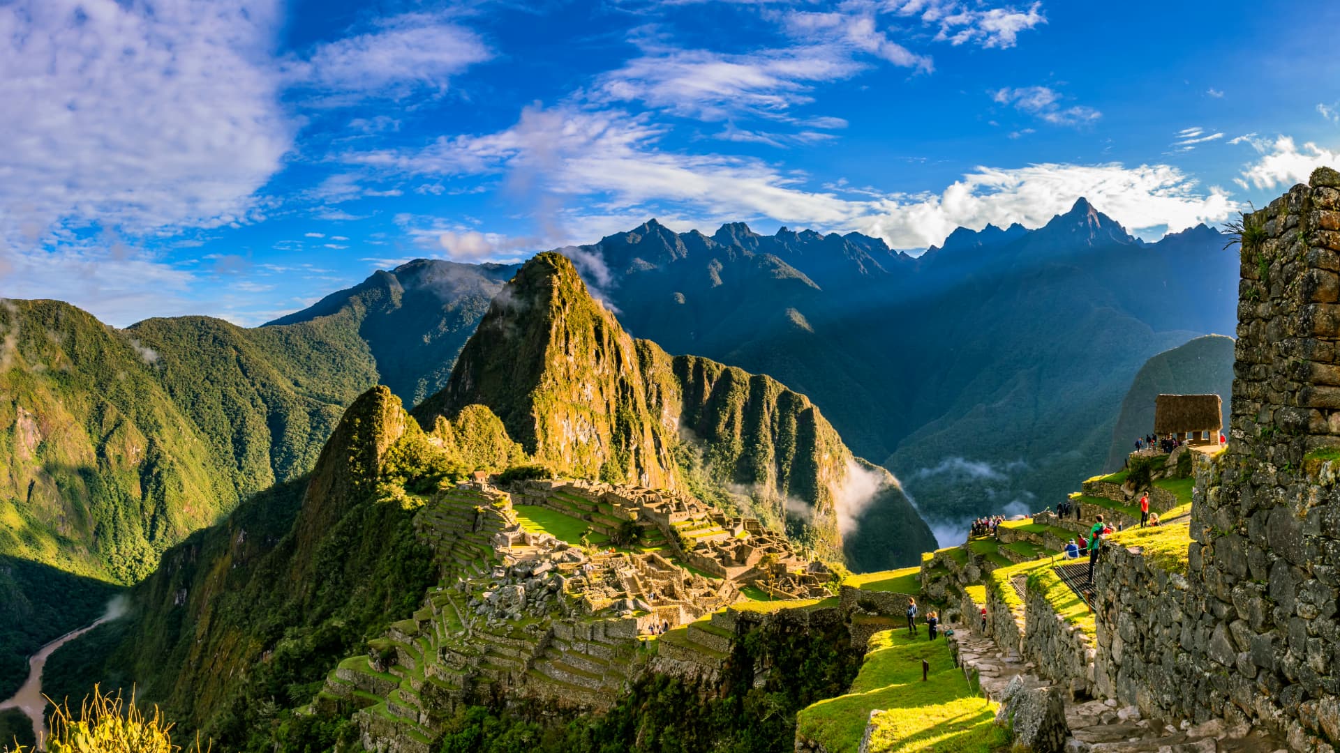 Panoramic shot of Machu Picchu with lush green mountains and a bright sky, showcasing the Inca ruins and surrounding Andes - Inka Trail Peru.info