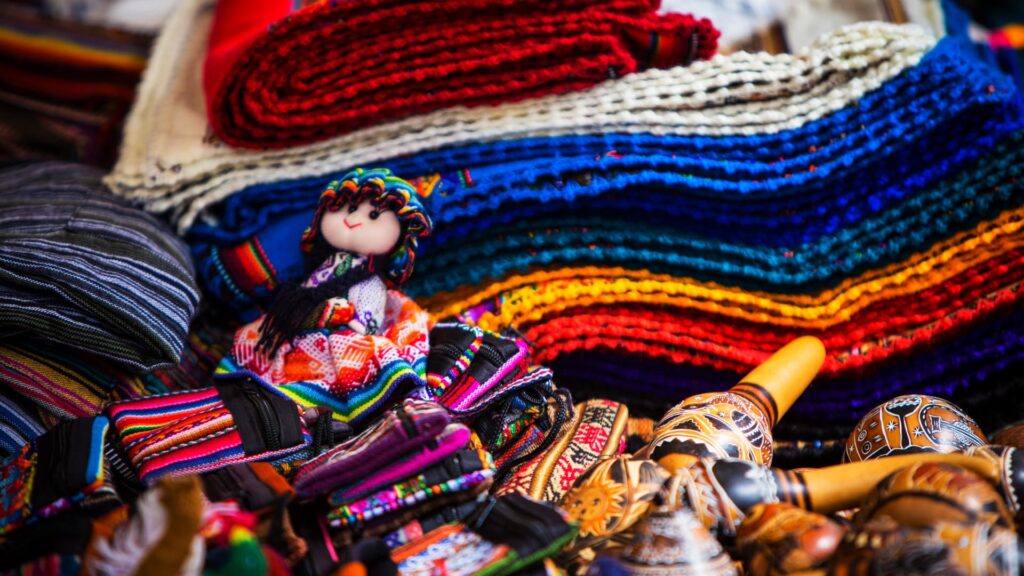A vibrant display of traditional Andean handicrafts at Mercado de San Pedro in Cusco, featuring colorful textiles, dolls, and carved gourds