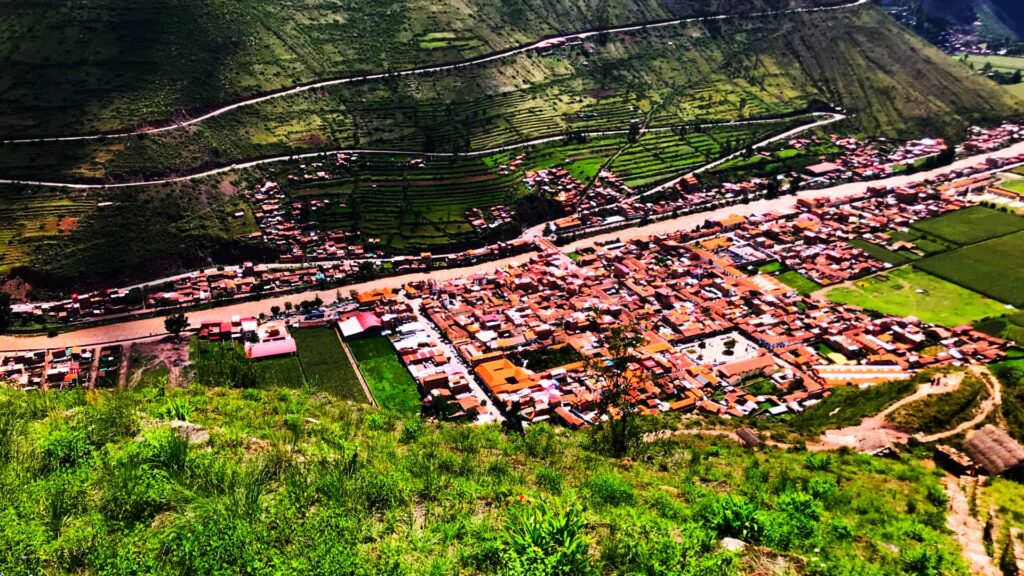 A breathtaking aerial view of a town in the Sacred Valley of the Incas, surrounded by lush green mountains and agricultural terraces