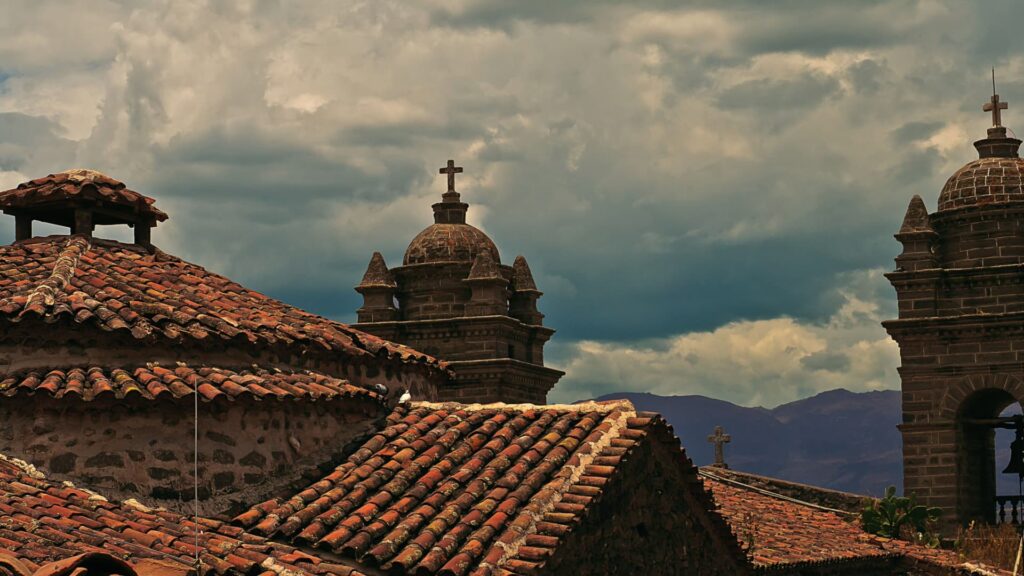 Colonial church rooftops and stone bell towers with crosses in Cusco under dramatic cloudy skies - Inka Trail Peru.info