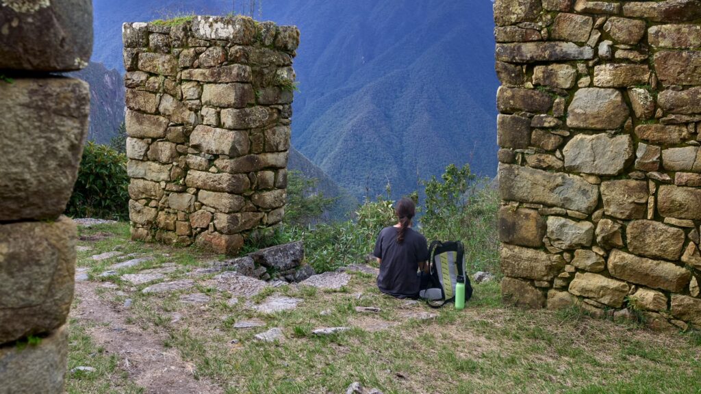 A solo hiker rests near ancient stone walls overlooking lush Andean mountains along the Inca Trail to Machu Picchu - Inka Trail Peru.info