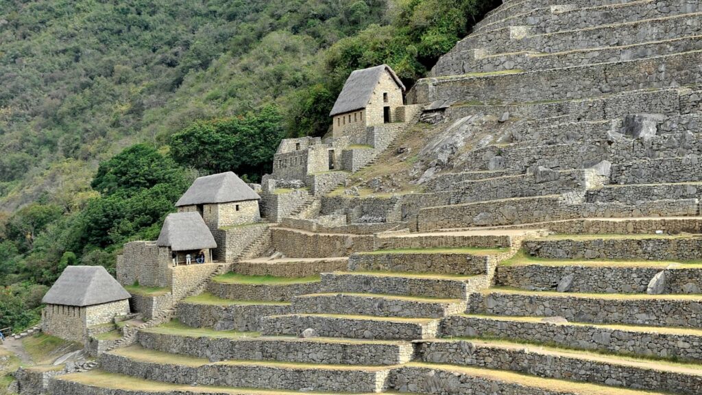 Tourists walking along the agricultural terraces of Machu Picchu, surrounded by lush green mountain scenery - Inka Trail Peru.info