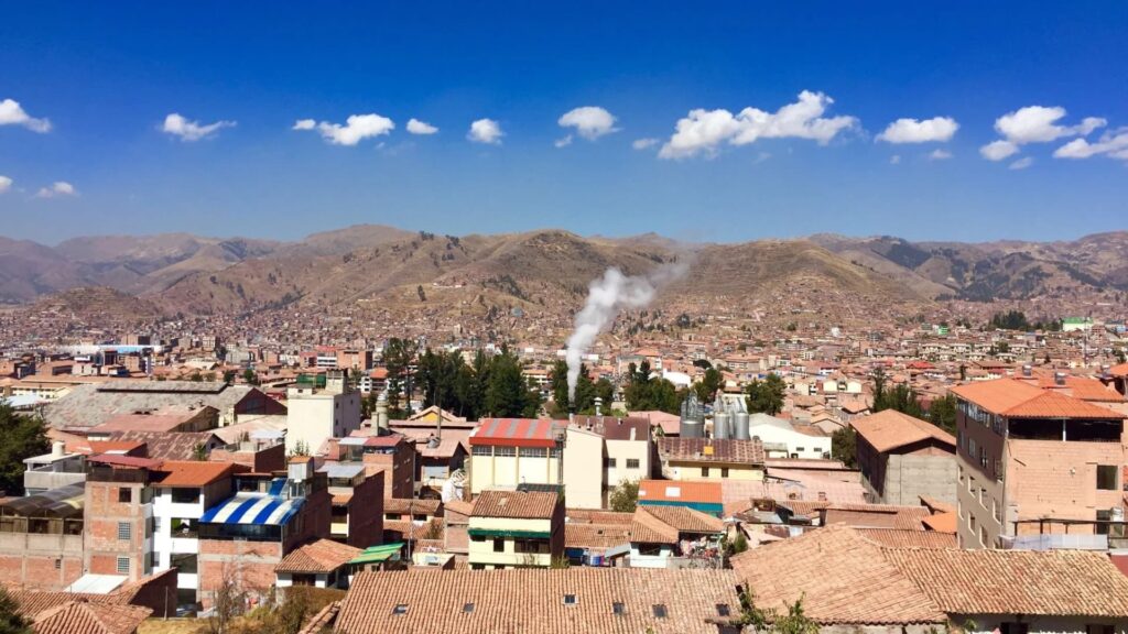 Panoramic view of Cusco with red-tile rooftops, Andean mountains and clear blue sky - IncaTrailPeru.info
