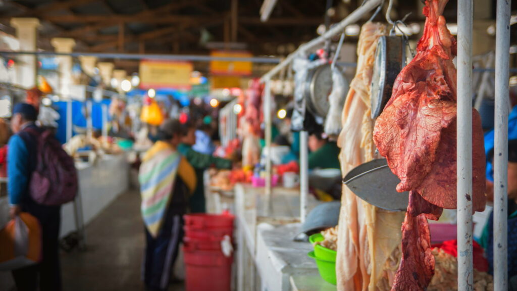Hanging cuts of meat and busy local vendors in a traditional Cusco market - Inka Trail Peru.info