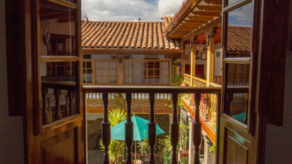 Balcony view of a colonial-style Cusco courtyard with tiled roofs, wooden railings, and a green umbrella in the center - IncaTrailPeru.info